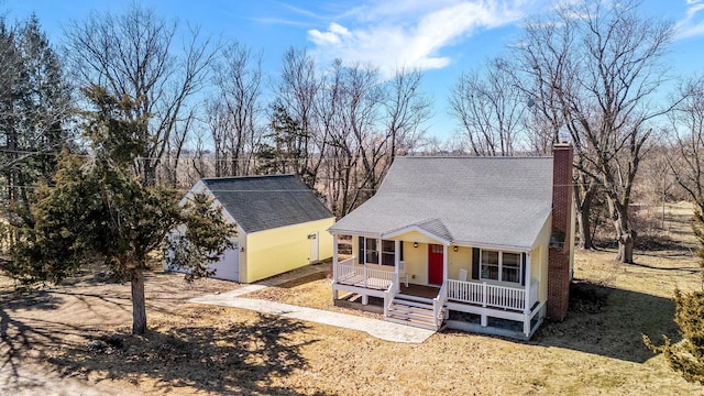 view of front of house with a porch, an outbuilding, roof with shingles, and a chimney