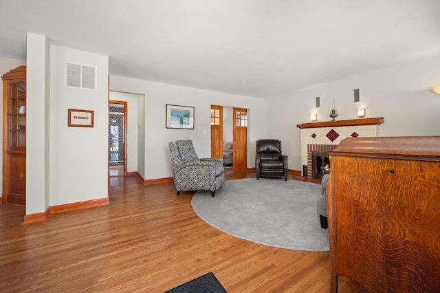 living area with visible vents, baseboards, a brick fireplace, and light wood finished floors