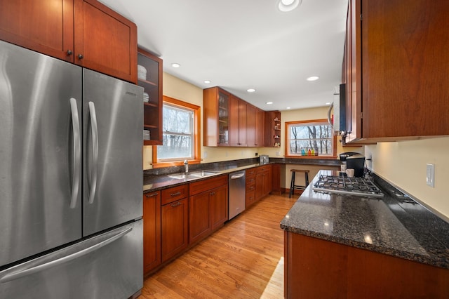 kitchen with light wood-type flooring, recessed lighting, dark stone countertops, appliances with stainless steel finishes, and a sink