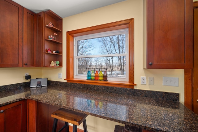 kitchen with open shelves, dark stone counters, and a breakfast bar area