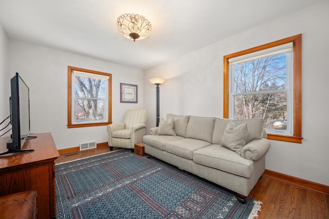 living area with a wealth of natural light, visible vents, baseboards, and wood finished floors