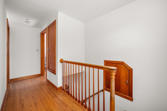 corridor featuring baseboards, an upstairs landing, and wood finished floors