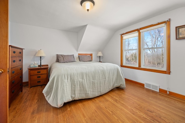 bedroom with visible vents, lofted ceiling, baseboards, and wood finished floors