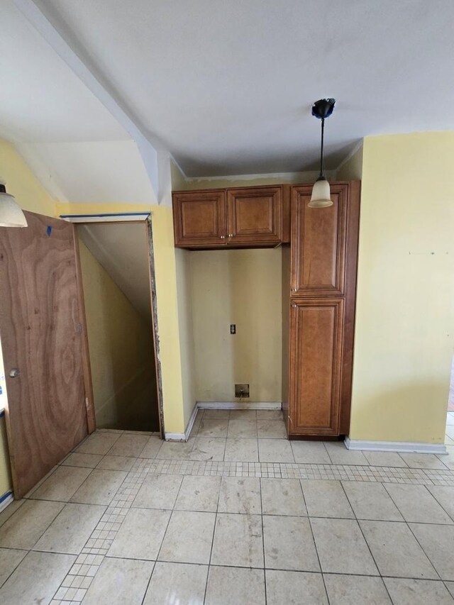 kitchen featuring light tile patterned flooring, hanging light fixtures, brown cabinetry, and baseboards