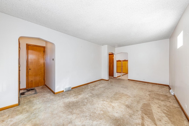 carpeted empty room featuring arched walkways, visible vents, a textured ceiling, and baseboards