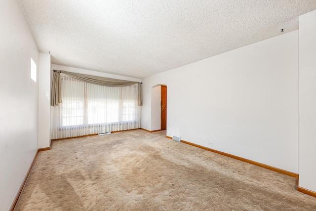 empty room featuring baseboards, arched walkways, carpet flooring, and a textured ceiling