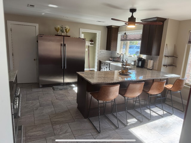 kitchen with visible vents, high end fridge, a sink, backsplash, and a peninsula