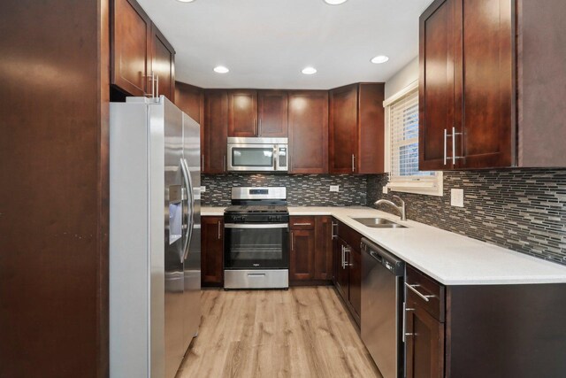 kitchen with light wood-style flooring, a sink, decorative backsplash, light countertops, and appliances with stainless steel finishes