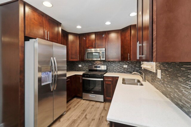 kitchen featuring light wood finished floors, a sink, light countertops, appliances with stainless steel finishes, and tasteful backsplash