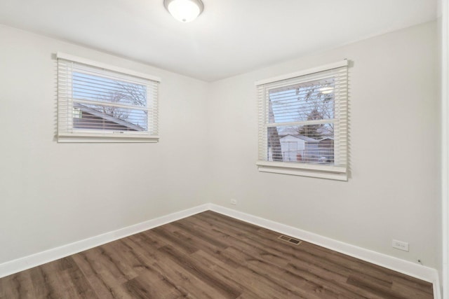 empty room with dark wood-style floors, baseboards, and visible vents