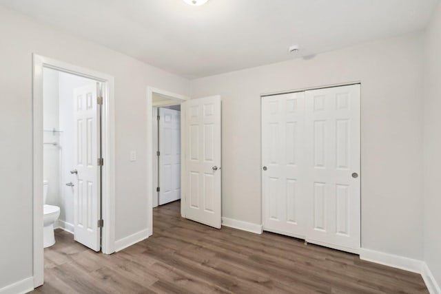 unfurnished bedroom with wood finished floors, baseboards, a closet, and connected bathroom