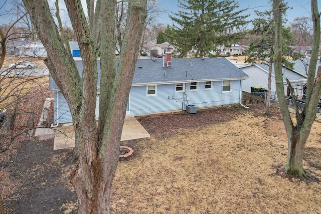 rear view of property with central air condition unit, a chimney, and a shingled roof