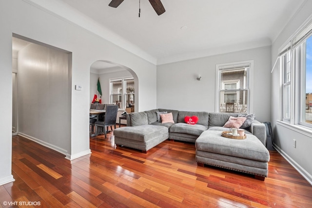 living area featuring baseboards, arched walkways, wood-type flooring, and a ceiling fan