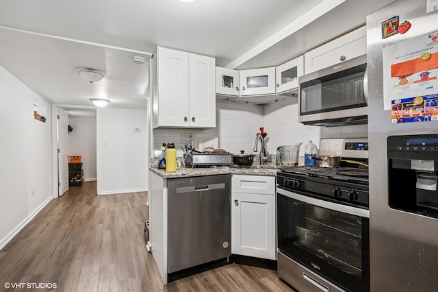 kitchen with light stone counters, backsplash, wood finished floors, appliances with stainless steel finishes, and white cabinets