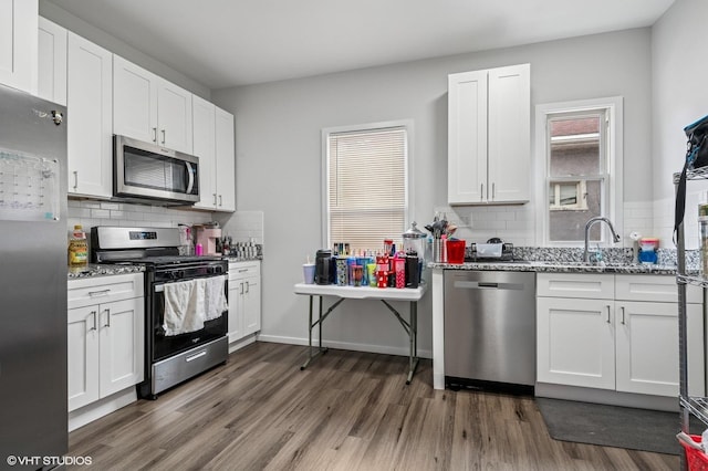 kitchen featuring light stone countertops, dark wood-style flooring, appliances with stainless steel finishes, white cabinetry, and backsplash