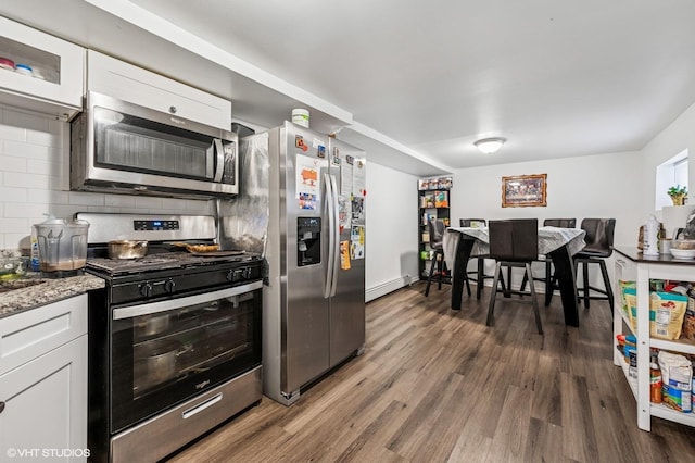 kitchen with backsplash, a baseboard heating unit, wood finished floors, white cabinets, and stainless steel appliances