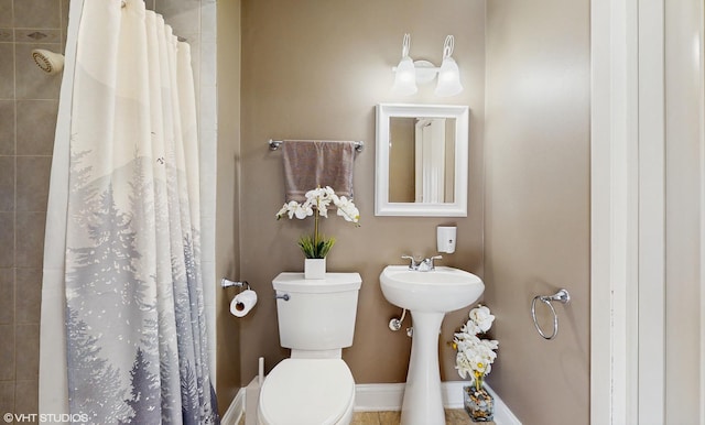 bathroom featuring tiled shower, toilet, and baseboards