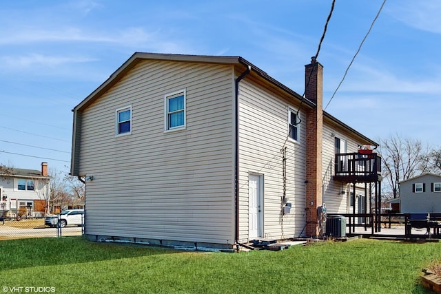 view of side of home with a balcony, a yard, fence, and a chimney