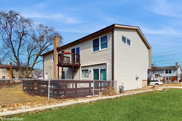 back of house featuring a balcony, a chimney, a lawn, and fence