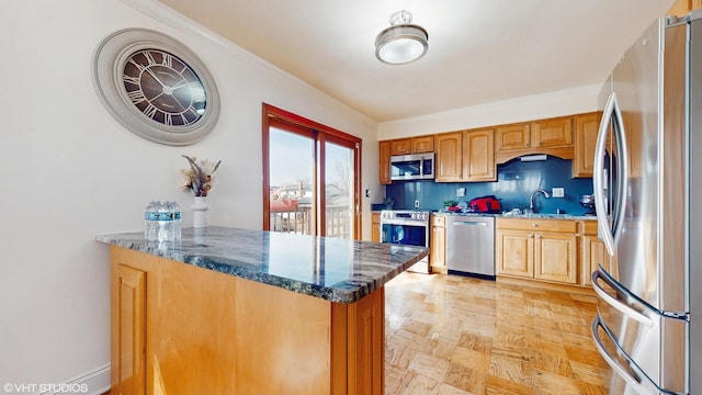 kitchen with crown molding, dark stone counters, a peninsula, stainless steel appliances, and a sink