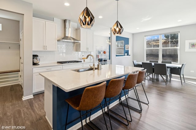 kitchen featuring gas cooktop, dark wood finished floors, a sink, wall chimney range hood, and tasteful backsplash