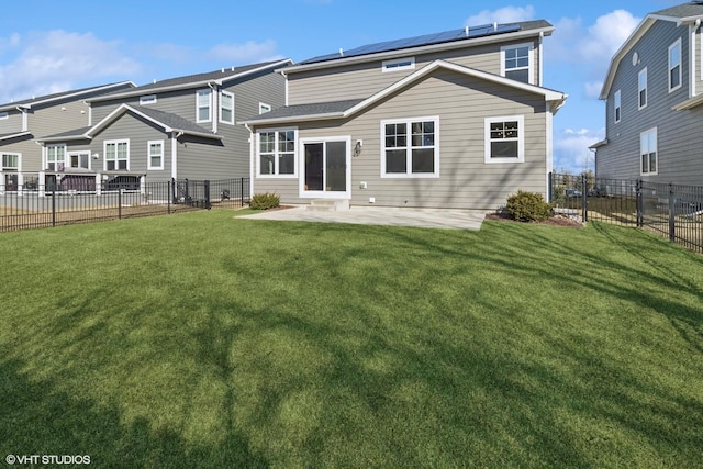 rear view of house with roof mounted solar panels, a lawn, a patio, and a fenced backyard