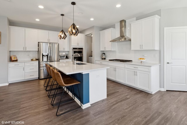 kitchen featuring appliances with stainless steel finishes, dark wood-type flooring, wall chimney range hood, and a sink