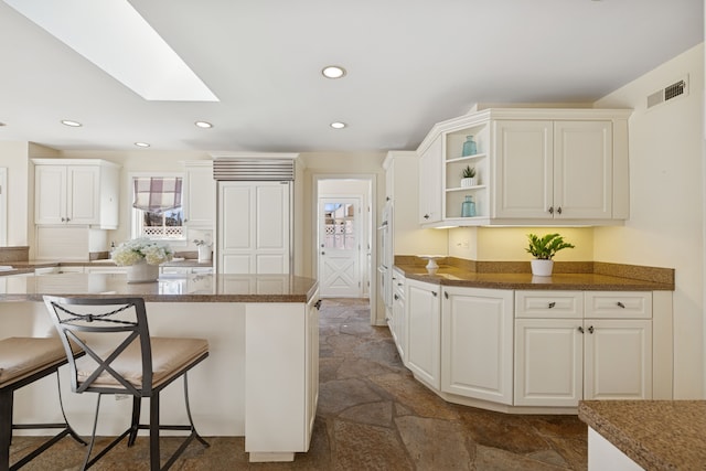 kitchen featuring visible vents, stone finish floor, a kitchen breakfast bar, and a skylight