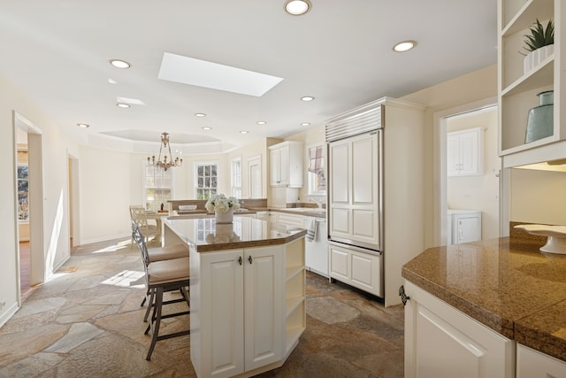 kitchen featuring stone tile flooring, recessed lighting, a breakfast bar area, white cabinets, and a raised ceiling