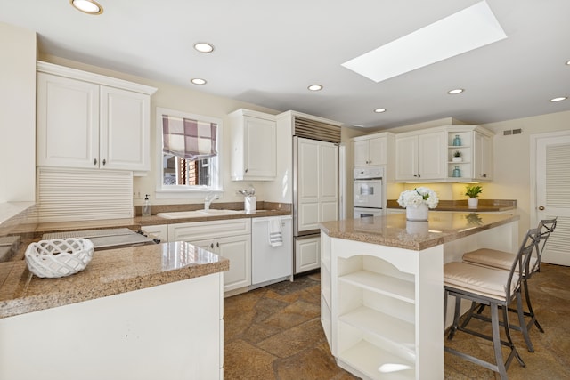 kitchen with a breakfast bar, stone finish floor, open shelves, a sink, and a skylight