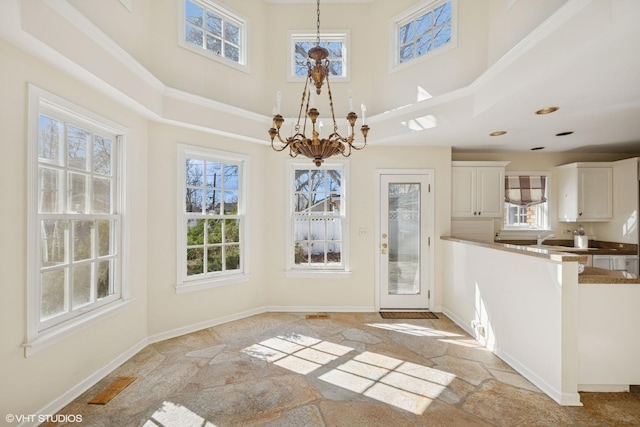 unfurnished dining area with visible vents, baseboards, a high ceiling, crown molding, and a chandelier