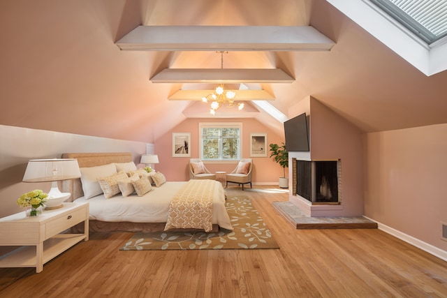 bedroom with lofted ceiling with skylight, wood finished floors, a multi sided fireplace, an inviting chandelier, and baseboards