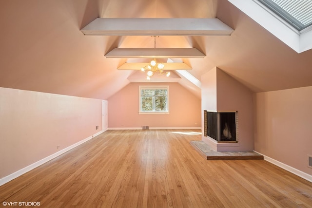 additional living space featuring visible vents, lofted ceiling with skylight, wood finished floors, baseboards, and a chandelier