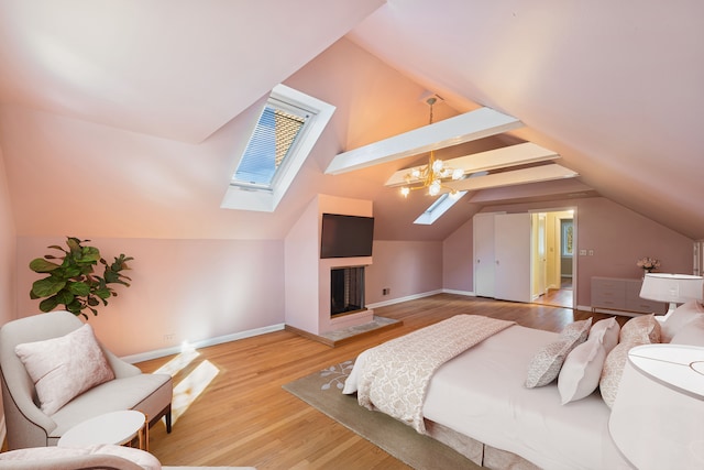 bedroom featuring lofted ceiling with skylight, a fireplace with raised hearth, light wood-type flooring, and baseboards