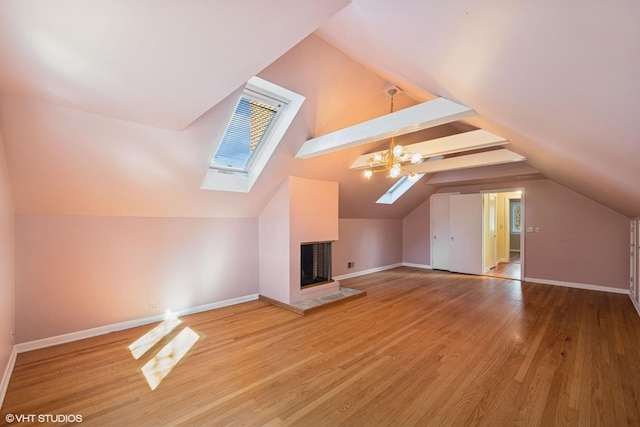 additional living space featuring vaulted ceiling with skylight, wood finished floors, baseboards, and a fireplace with raised hearth