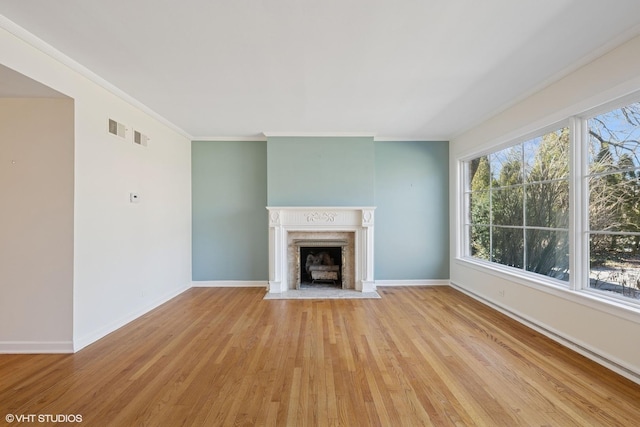 unfurnished living room with crown molding, baseboards, light wood-type flooring, and a high end fireplace