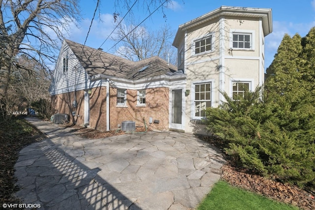 back of property featuring a patio area, brick siding, central AC, and stucco siding