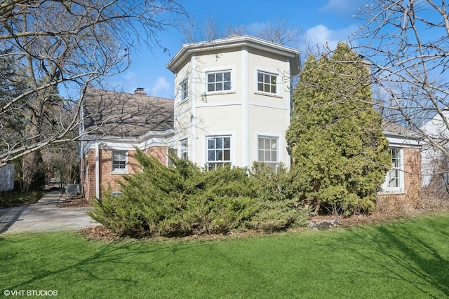 view of property exterior featuring brick siding, stucco siding, and a yard