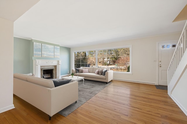 living room featuring wood finished floors, a fireplace, crown molding, baseboards, and stairs