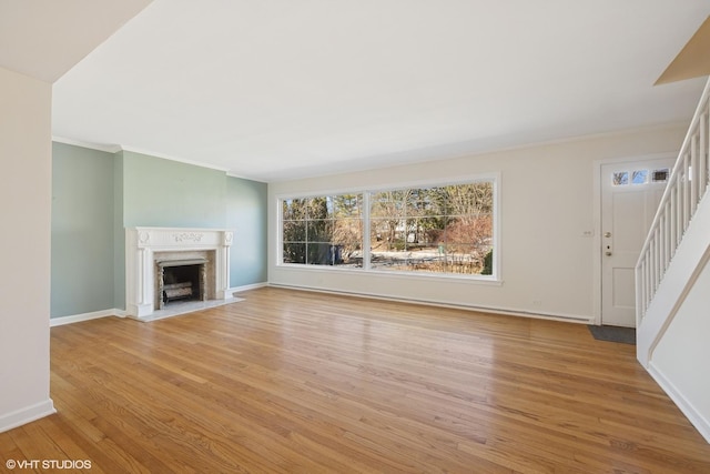 unfurnished living room featuring stairs, light wood-style flooring, baseboards, and a high end fireplace