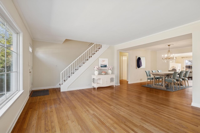 unfurnished living room featuring stairway, light wood-style floors, crown molding, baseboards, and a chandelier