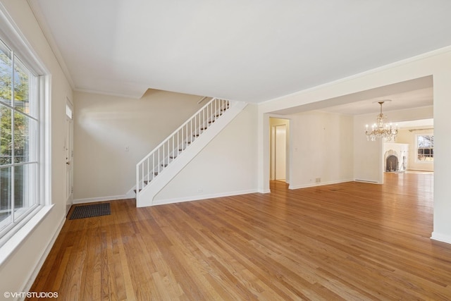 unfurnished living room featuring baseboards, stairs, ornamental molding, an inviting chandelier, and light wood-style floors