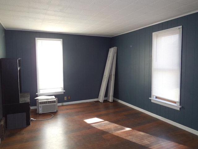 empty room featuring an AC wall unit, crown molding, wood finished floors, and baseboards