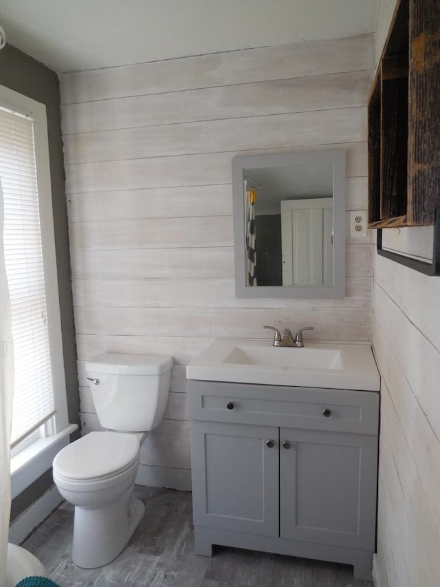 half bath with wooden walls, toilet, and vanity