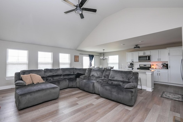 living room featuring ceiling fan with notable chandelier, high vaulted ceiling, baseboards, and wood finished floors