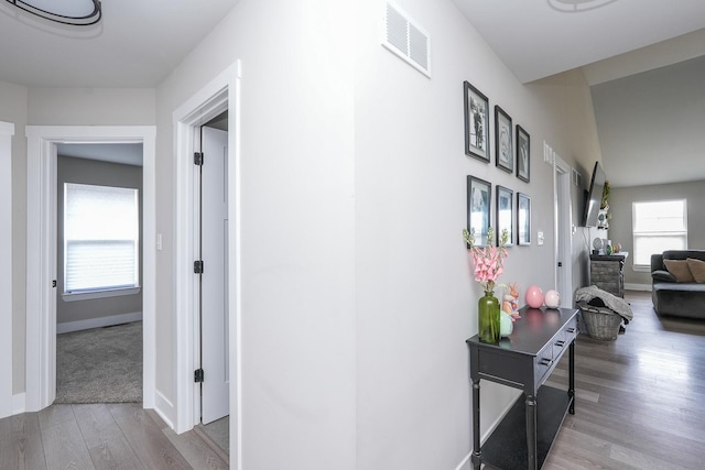 hallway featuring visible vents, baseboards, and wood finished floors