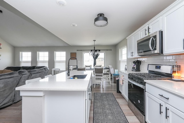 kitchen with a sink, backsplash, open floor plan, appliances with stainless steel finishes, and light countertops