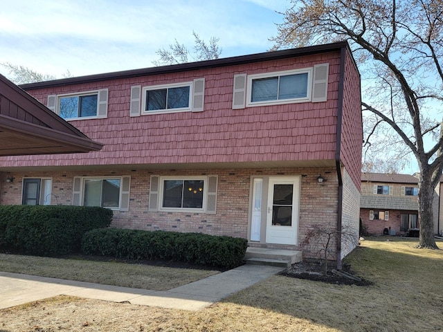 view of property featuring mansard roof, brick siding, and a front yard