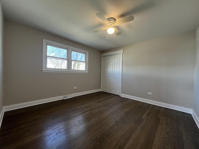 unfurnished bedroom with dark wood-style floors, baseboards, a closet, and ceiling fan