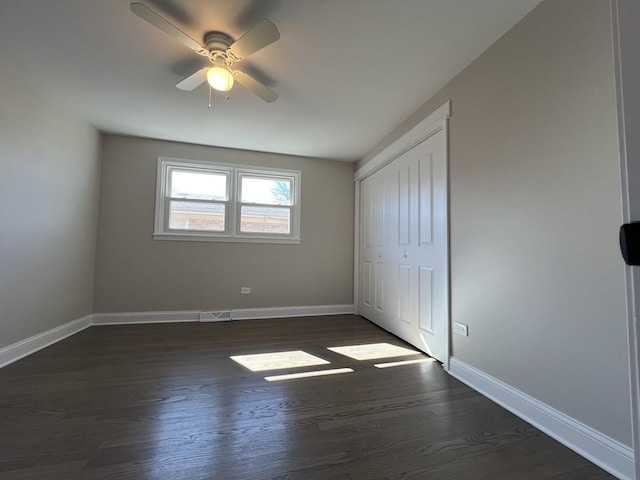 unfurnished bedroom with a closet, baseboards, dark wood-type flooring, and a ceiling fan